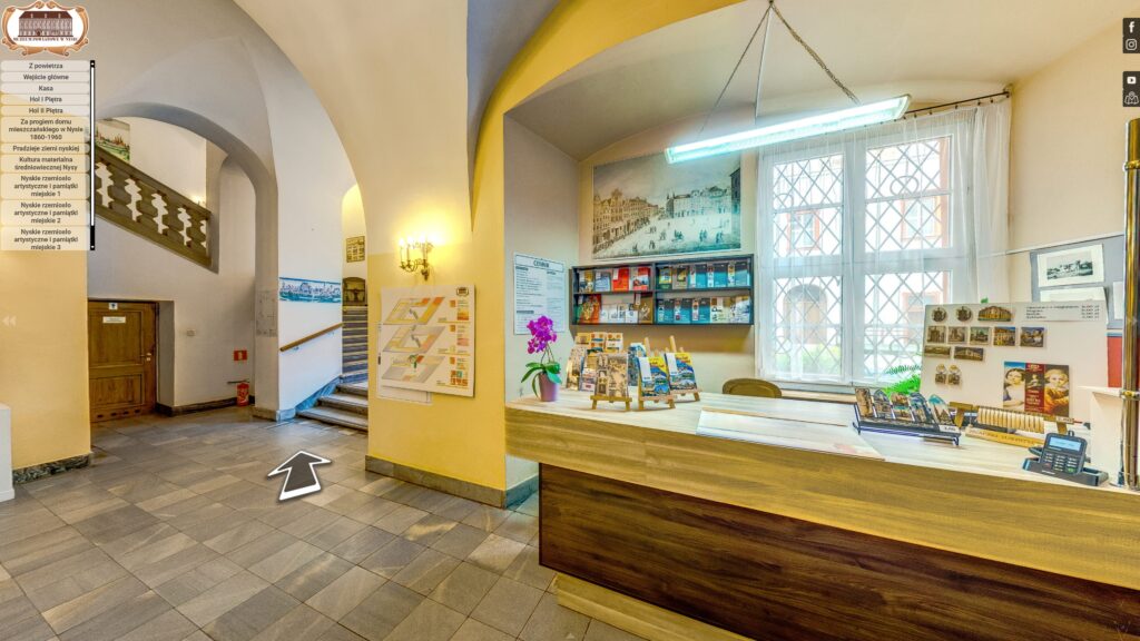Wnętrze wejścia do Muzeum Powiatowego w Nysie, przedstawiające recepcję, kasę biletową oraz plan muzeum, widoczne w wirtualnym spacerze 360.